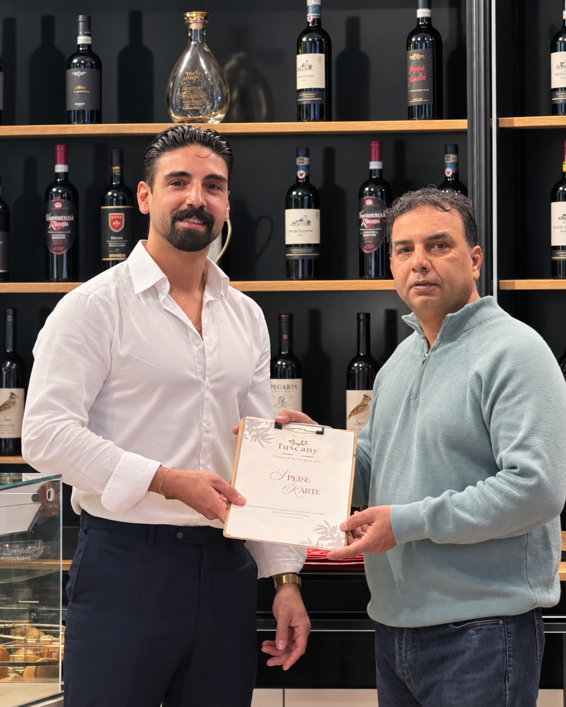 Miguel Herranz überreicht die fertige Speisekarte im Tuscany Restaurant vor dem Weinregal